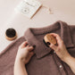 Person using a wooden brush on a brown garment with a white background