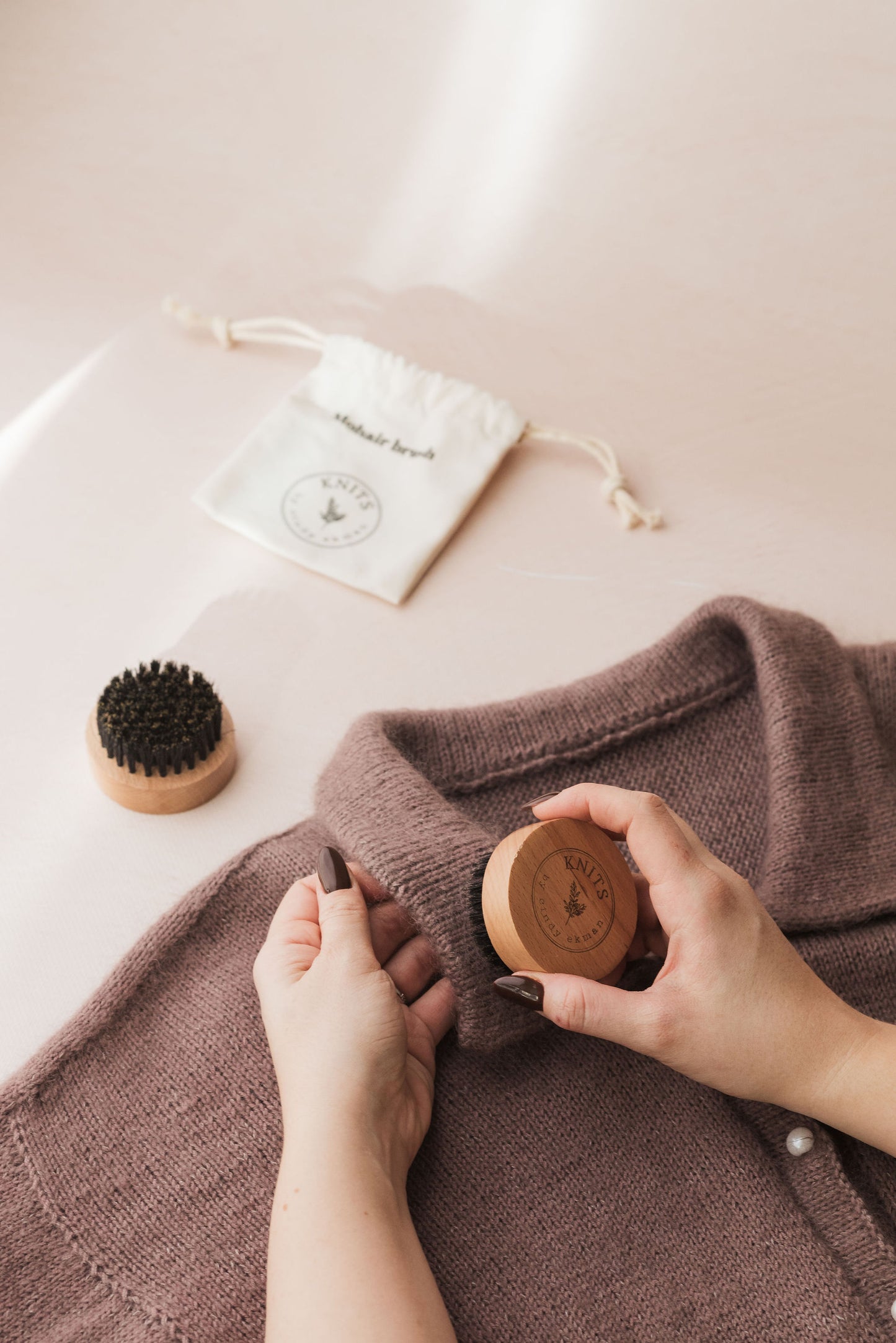 Person using a wooden garment brush on a brown sweater with a white drawstring bag in the background.