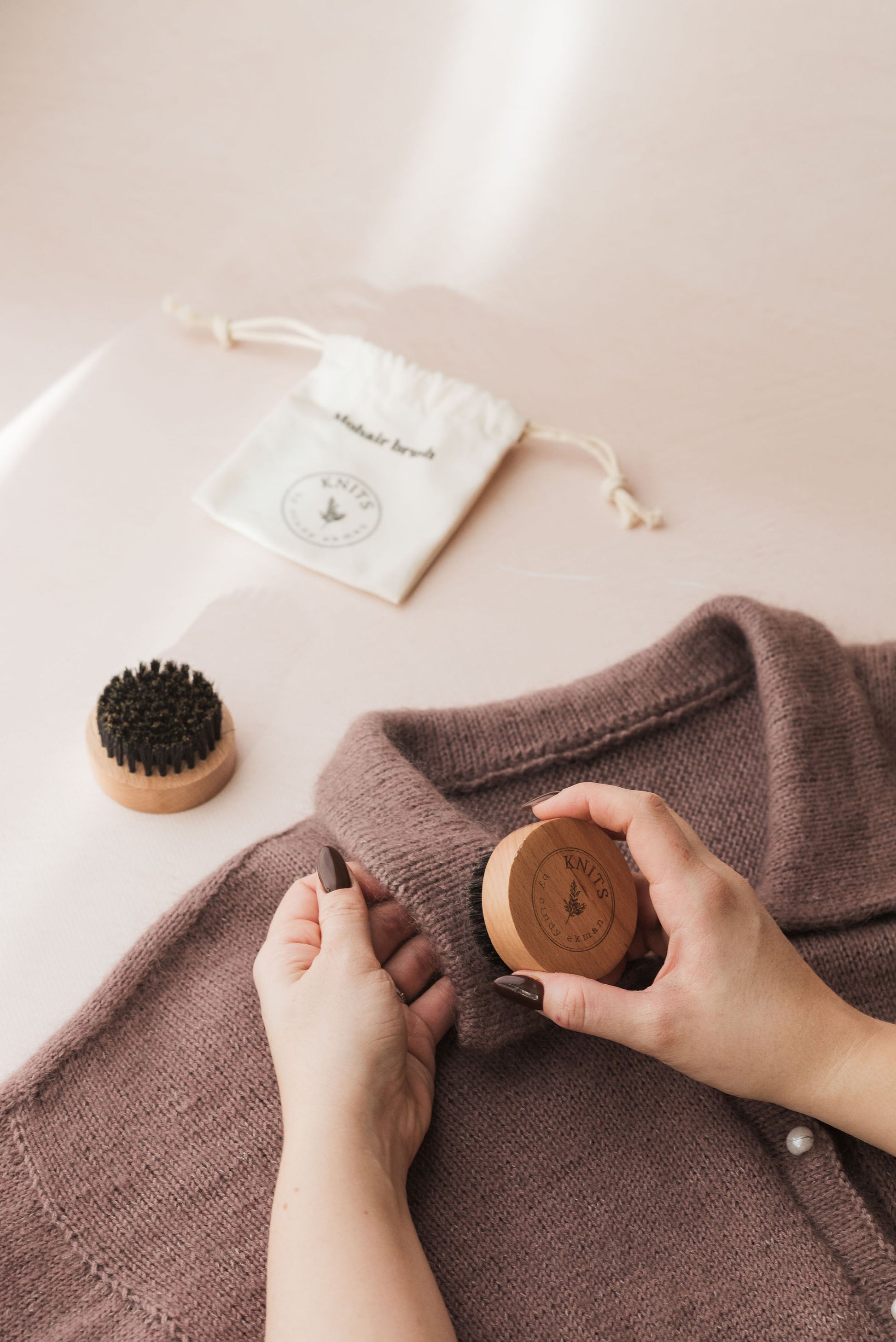 Person using a wooden garment brush on a brown sweater with a white drawstring bag in the background.