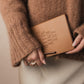Person wearing a brown sweater holding a brown leather notebook with 'EAT KNIT SLEEP' text.
