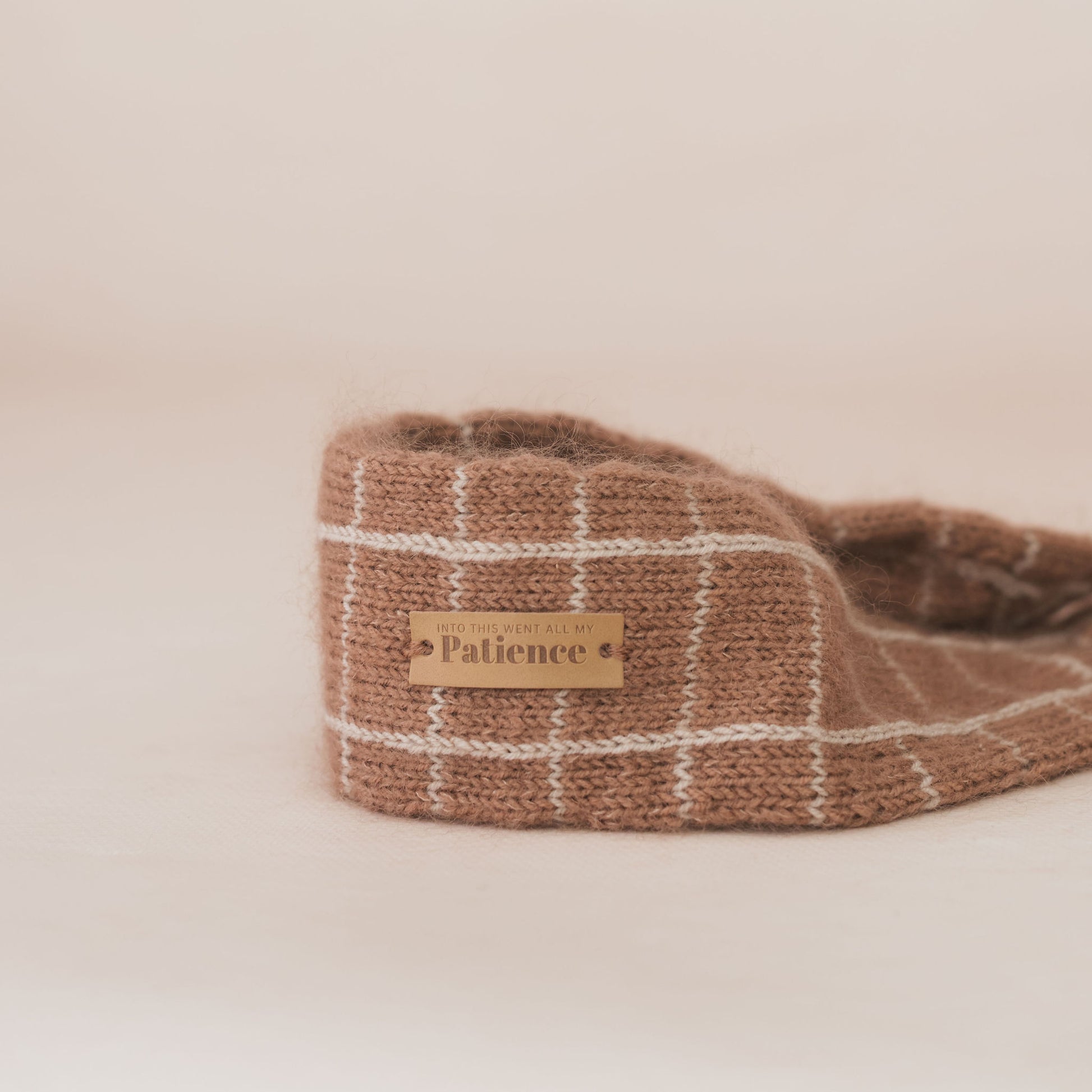 Knitted slipper with a 'Patience' label on a beige background