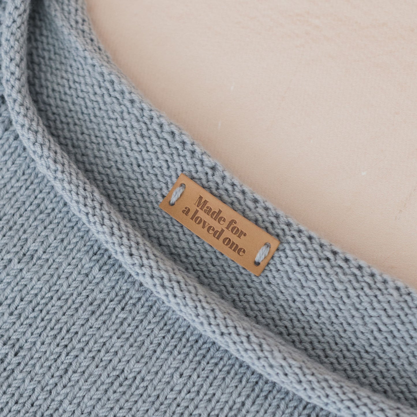 Gray knitted blanket with a label reading 'Made for a loved one' on a beige background