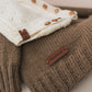 Close-up of a brown knitted garment with a 'Handmade' label, featuring another garment in the background.