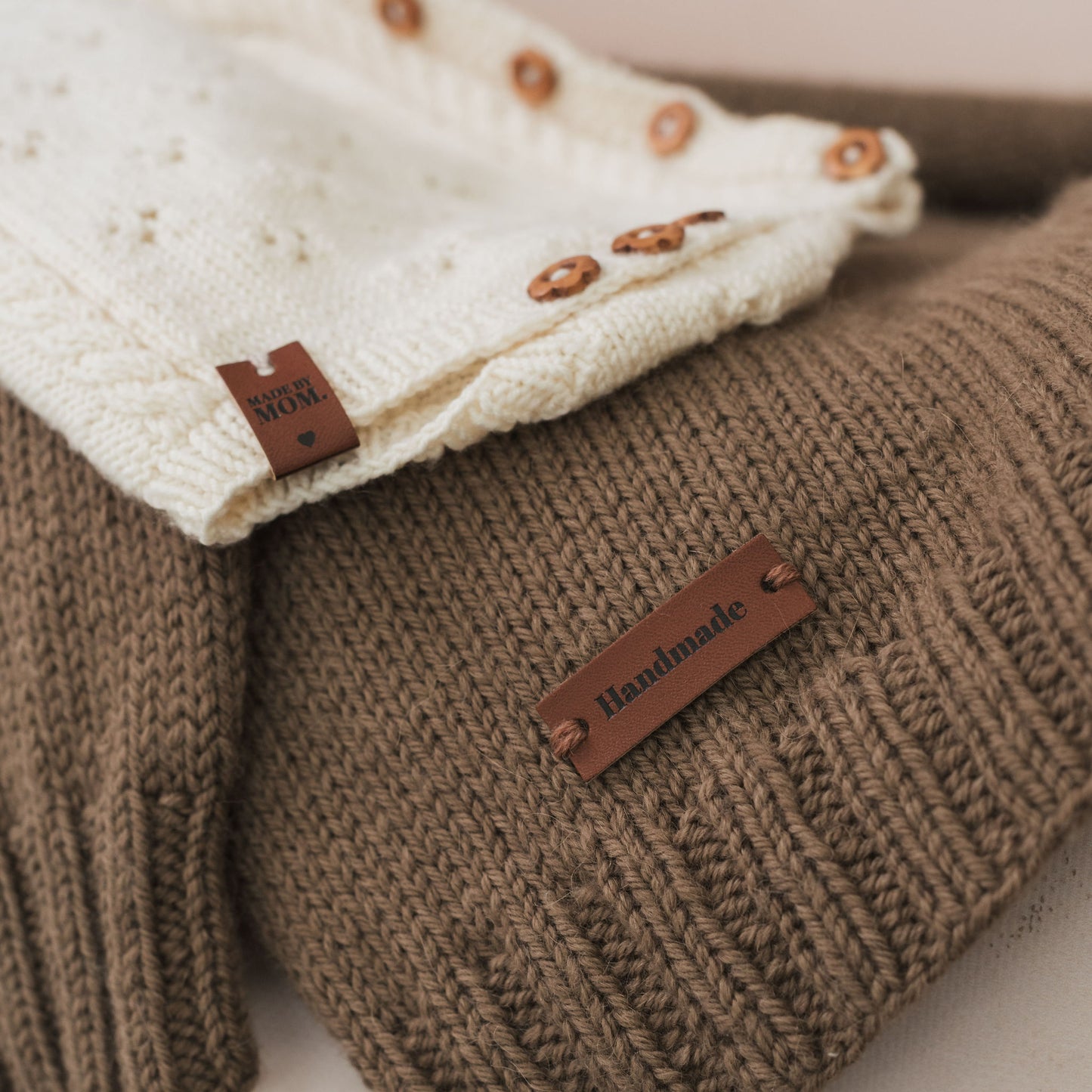 Close-up of a brown knitted garment with a 'Handmade' label, featuring another garment in the background.