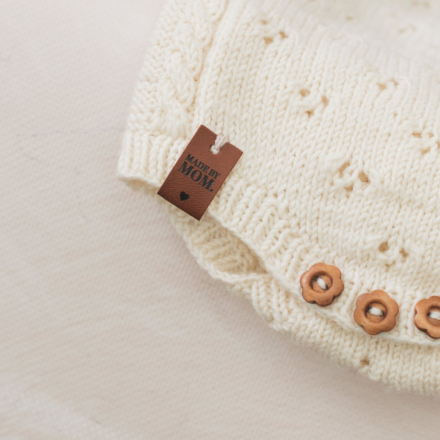 Close-up of a cream-colored knitted garment with a 'Made by Mom' label on a light background