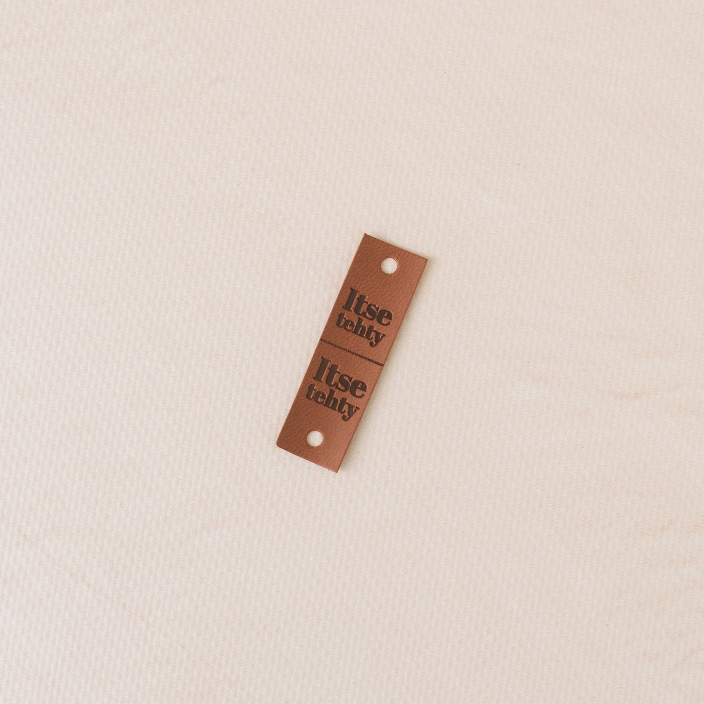 Brown leather tag with 'itse tehy' text on a beige background