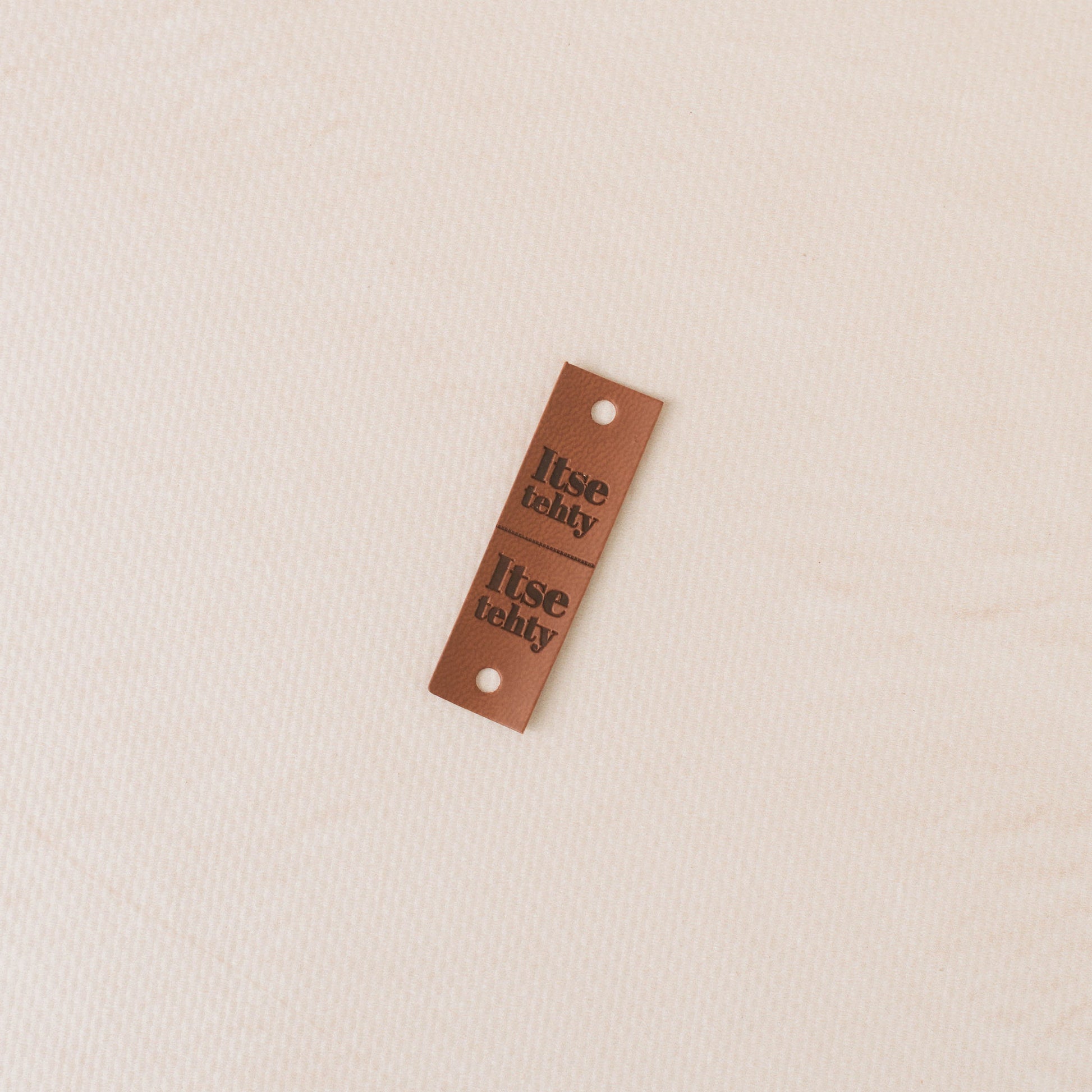 Brown leather tag with 'itse tehy' text on a beige background