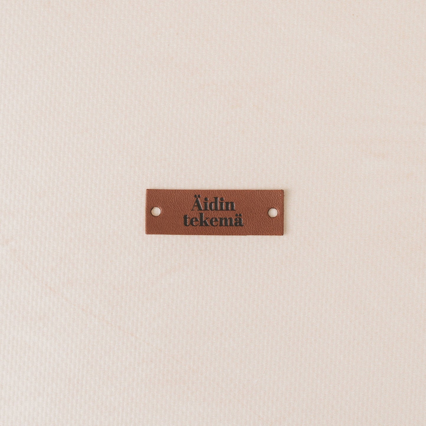 Brown leather label with text on a beige background, äidin tekemä