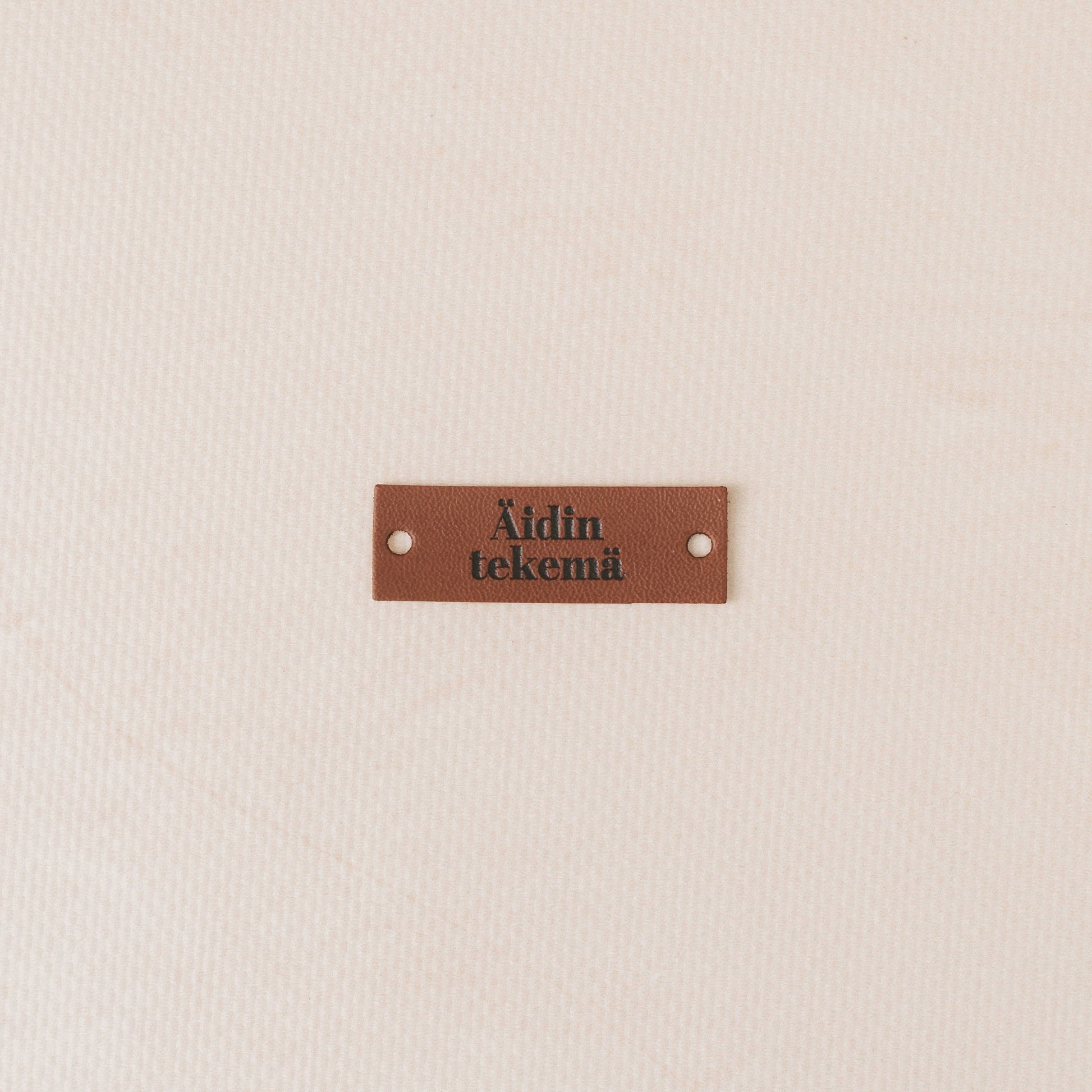 Brown leather label with text on a beige background, äidin tekemä