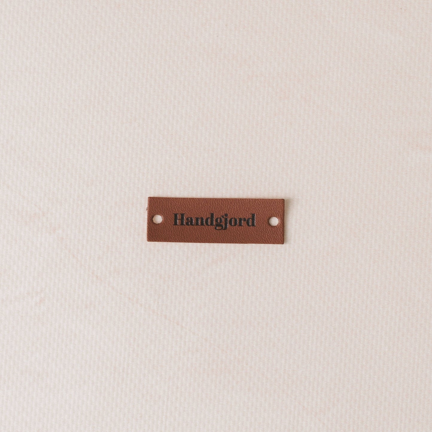 Brown leather label with 'Handgjord' text on a beige fabric background