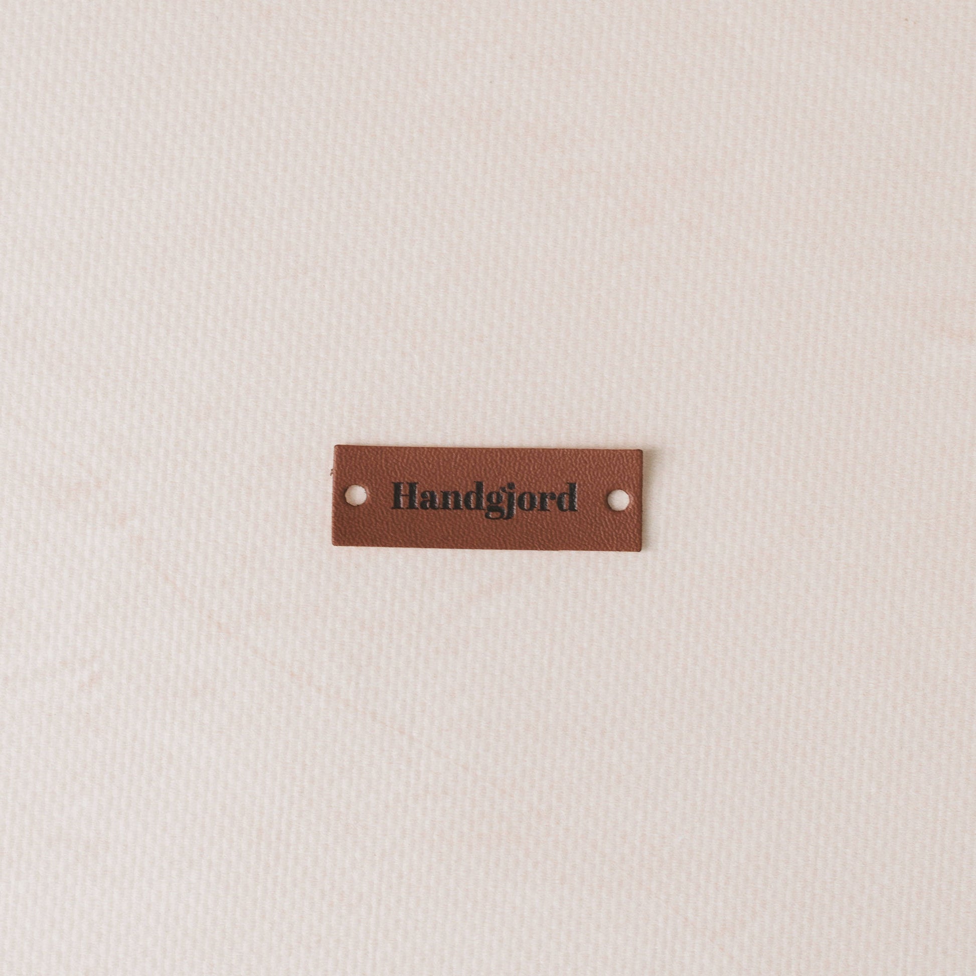 Brown leather label with 'Handgjord' text on a beige fabric background