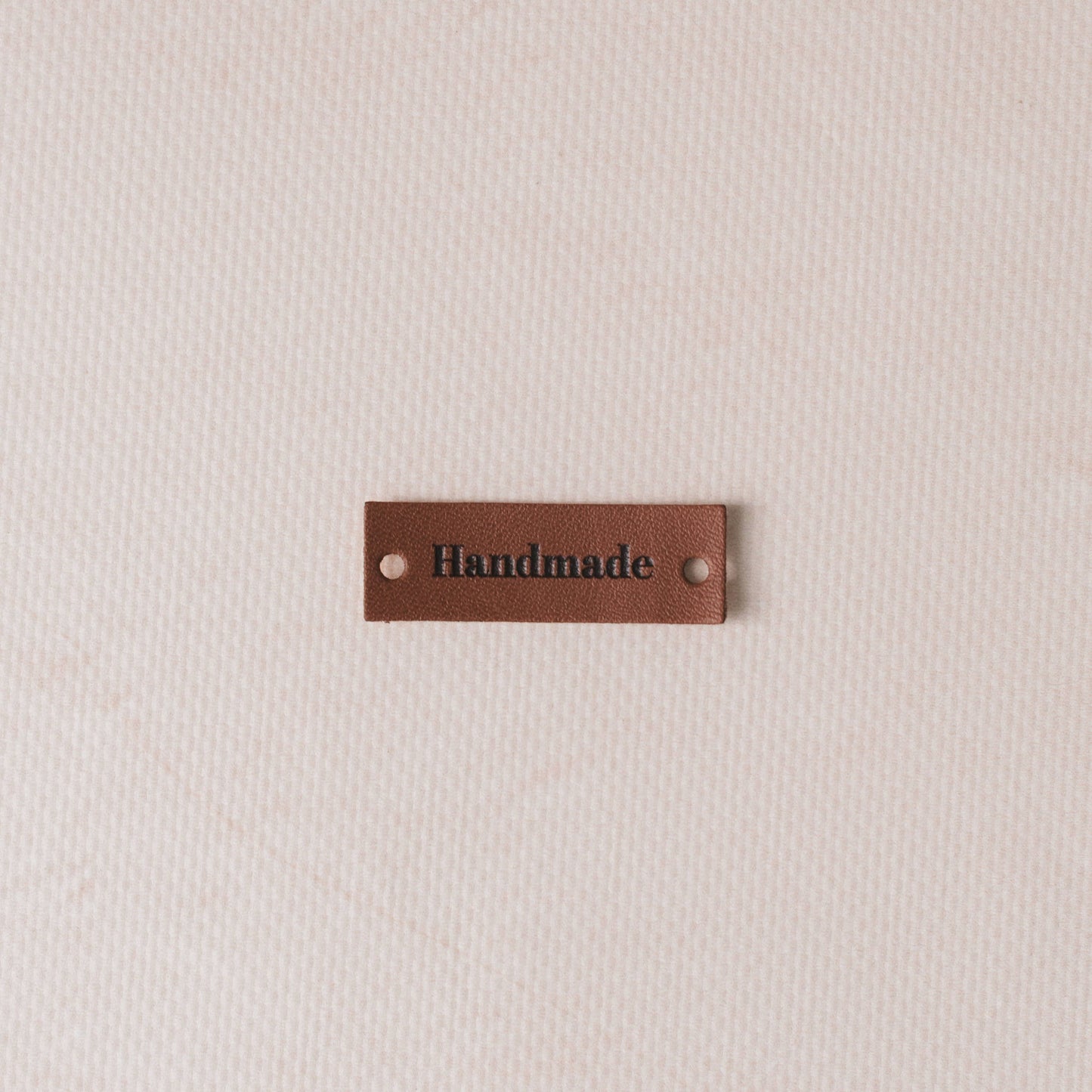 Brown leather label with 'Handmade' text on a beige fabric background