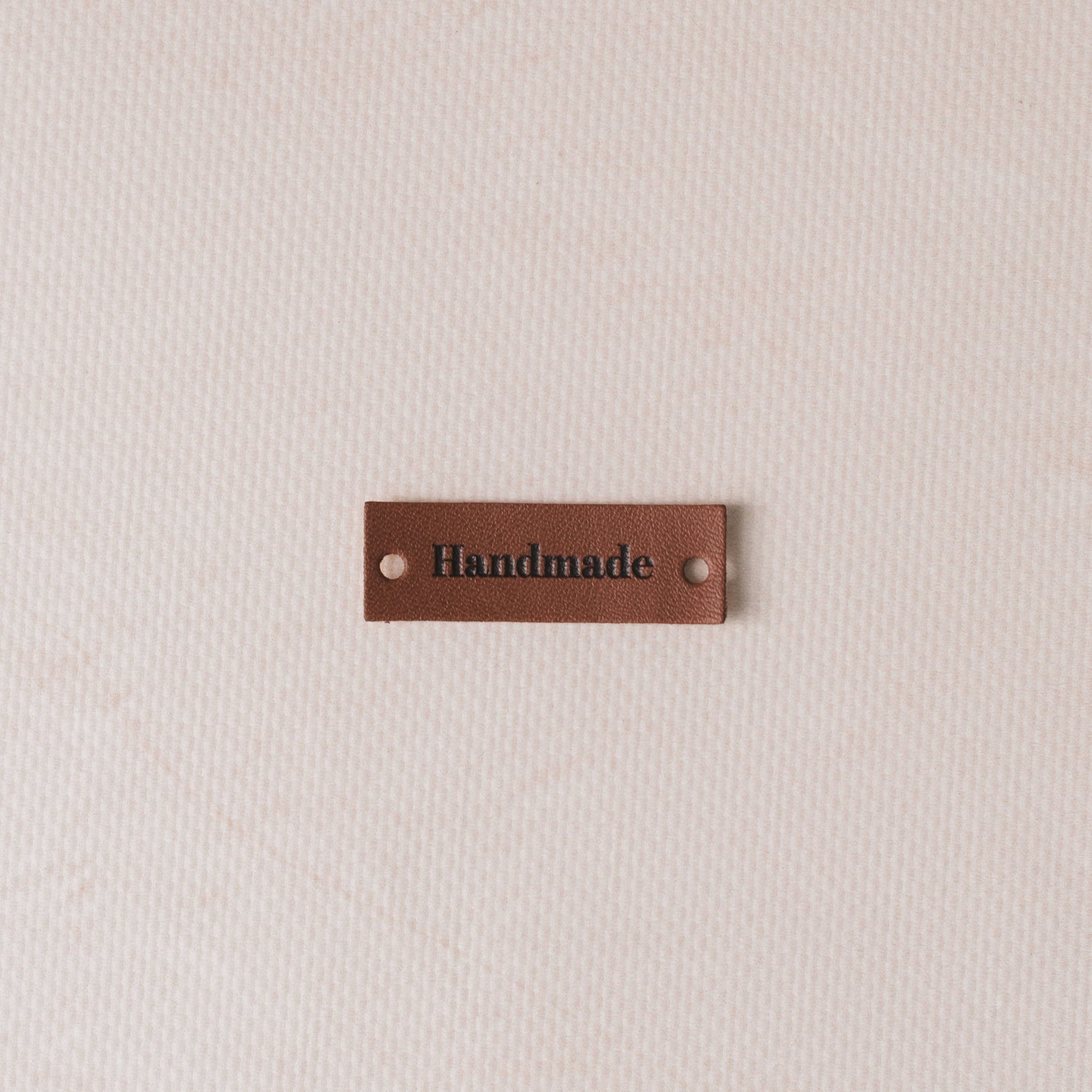 Brown leather label with 'Handmade' text on a beige fabric background