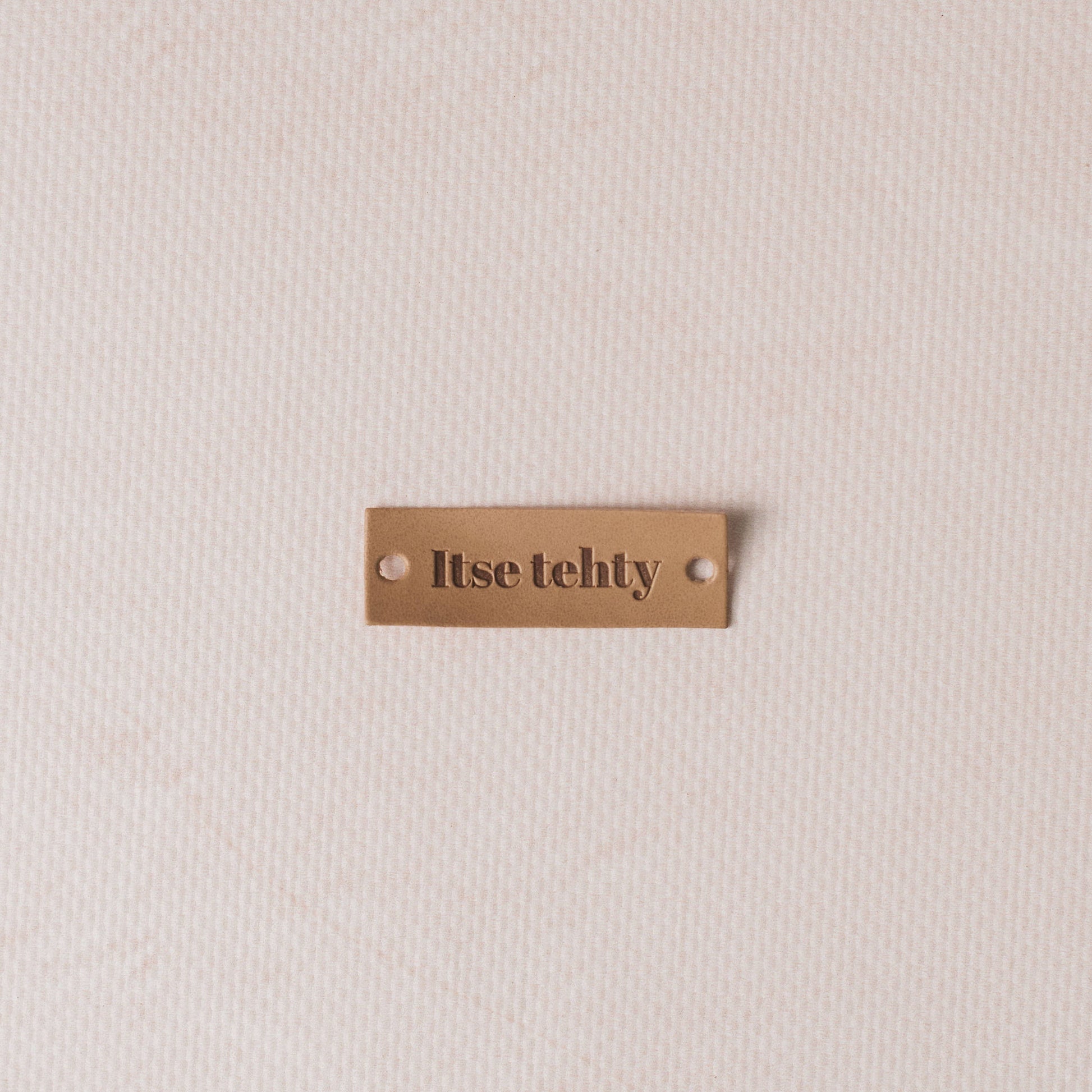 Tan coloured tag with 'Itse tehty' text on a beige background