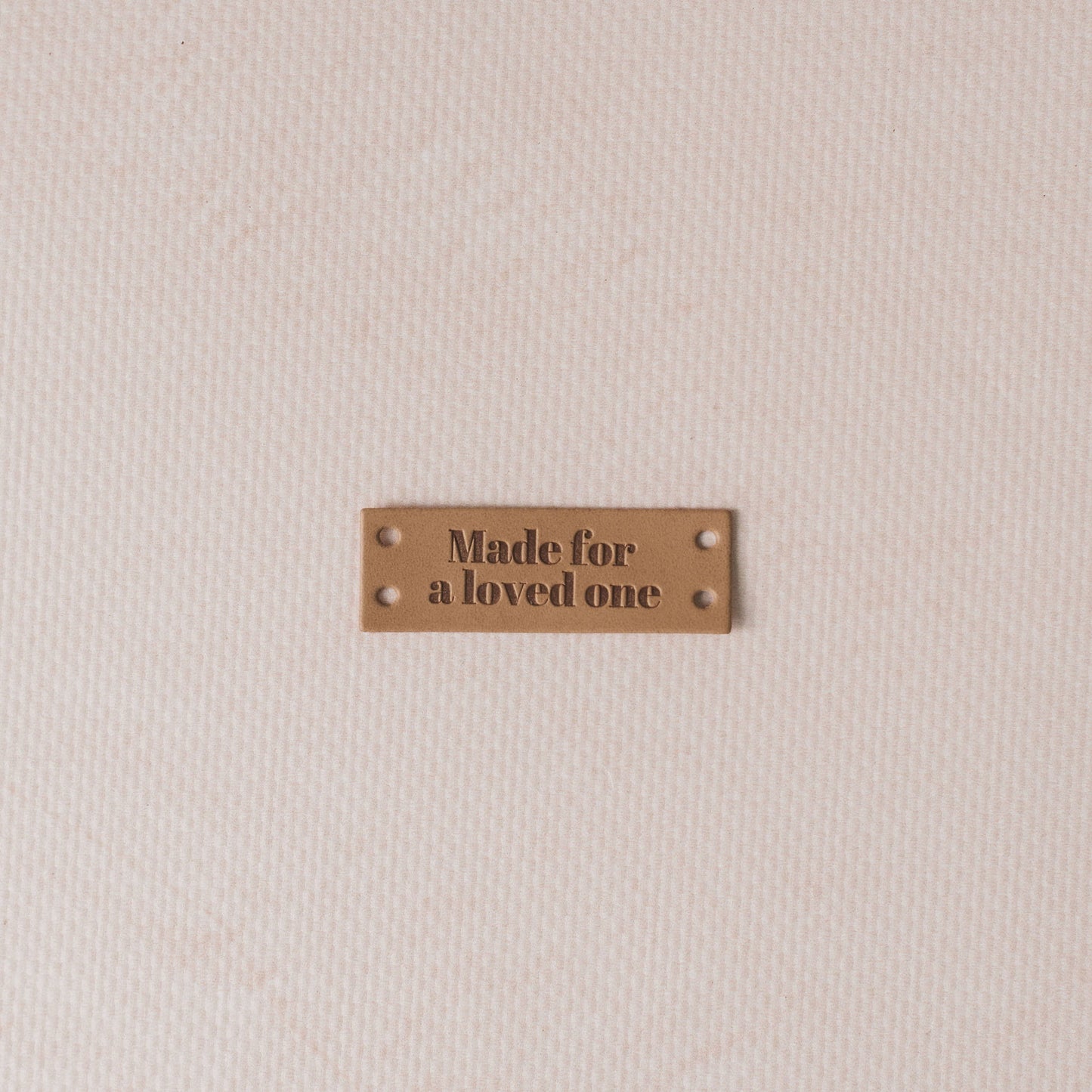 Brown leather label with 'Made for a loved one' text on a beige fabric background