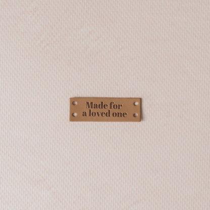 Brown leather label with 'Made for a loved one' text on a beige fabric background