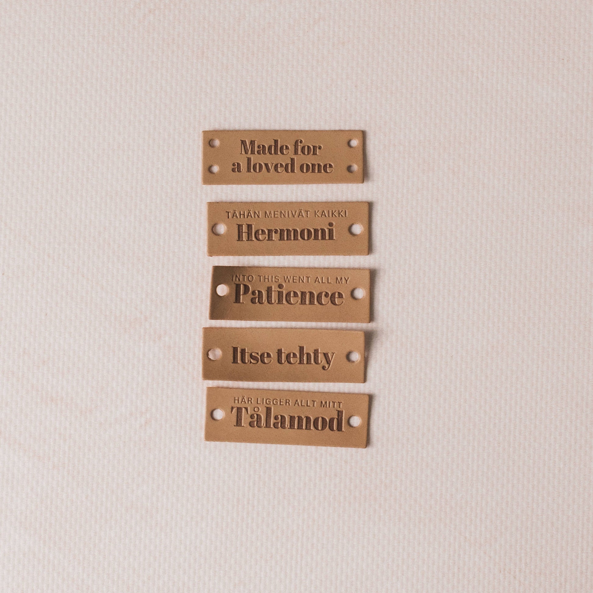 Set of five brown leather labels with engraved text on a beige background