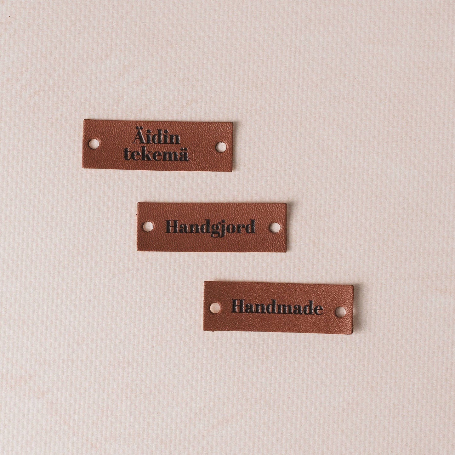 Three brown leather labels with engraved text on a beige background