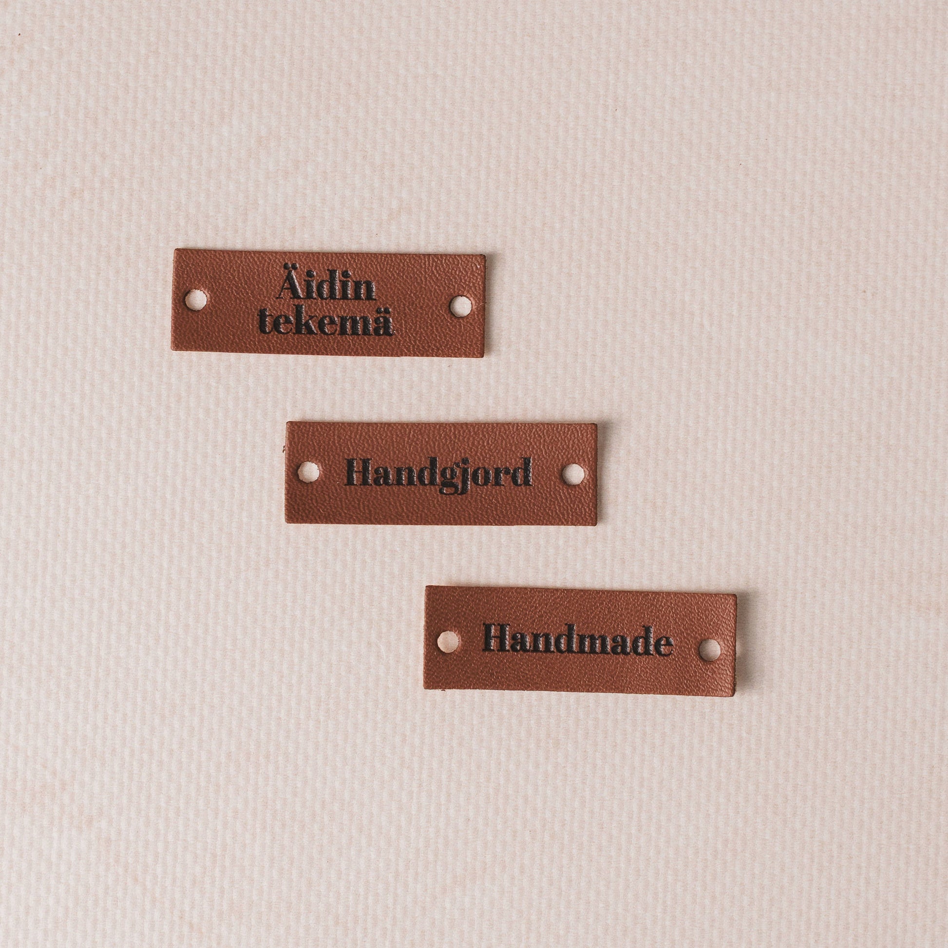 Three brown leather labels with engraved text on a beige background
