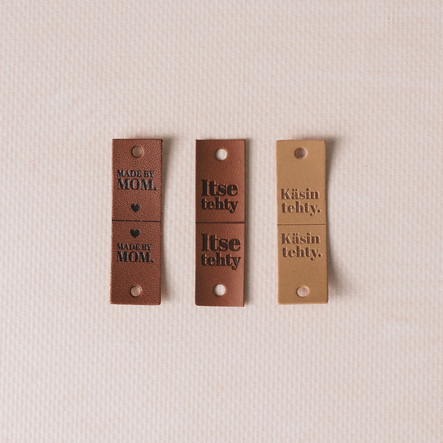 Three brown leather tags with text on a beige background