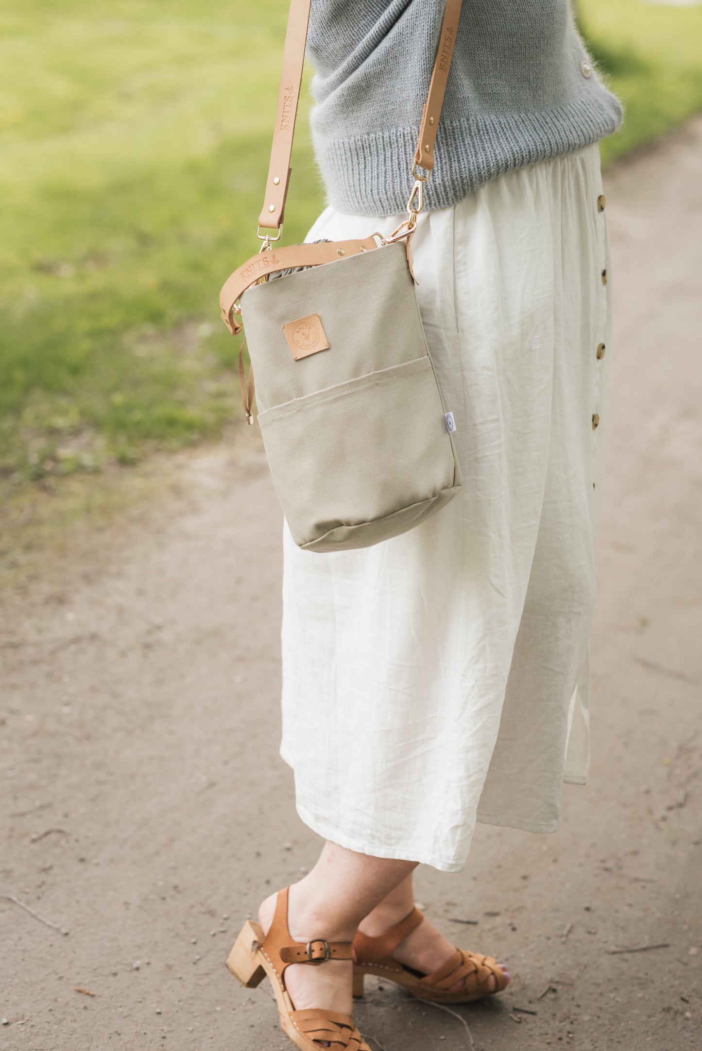 Person wearing a light green bag, white skirt, and brown shoes on a path.