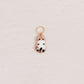 A small rose gold charm shaped like a cute white cat wearing a pink crown, resting on a textured off-white surface.