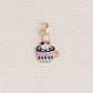 A small gold-tone charm shaped like a cupcake with colorful enamel details, photographed on a light textured background.
