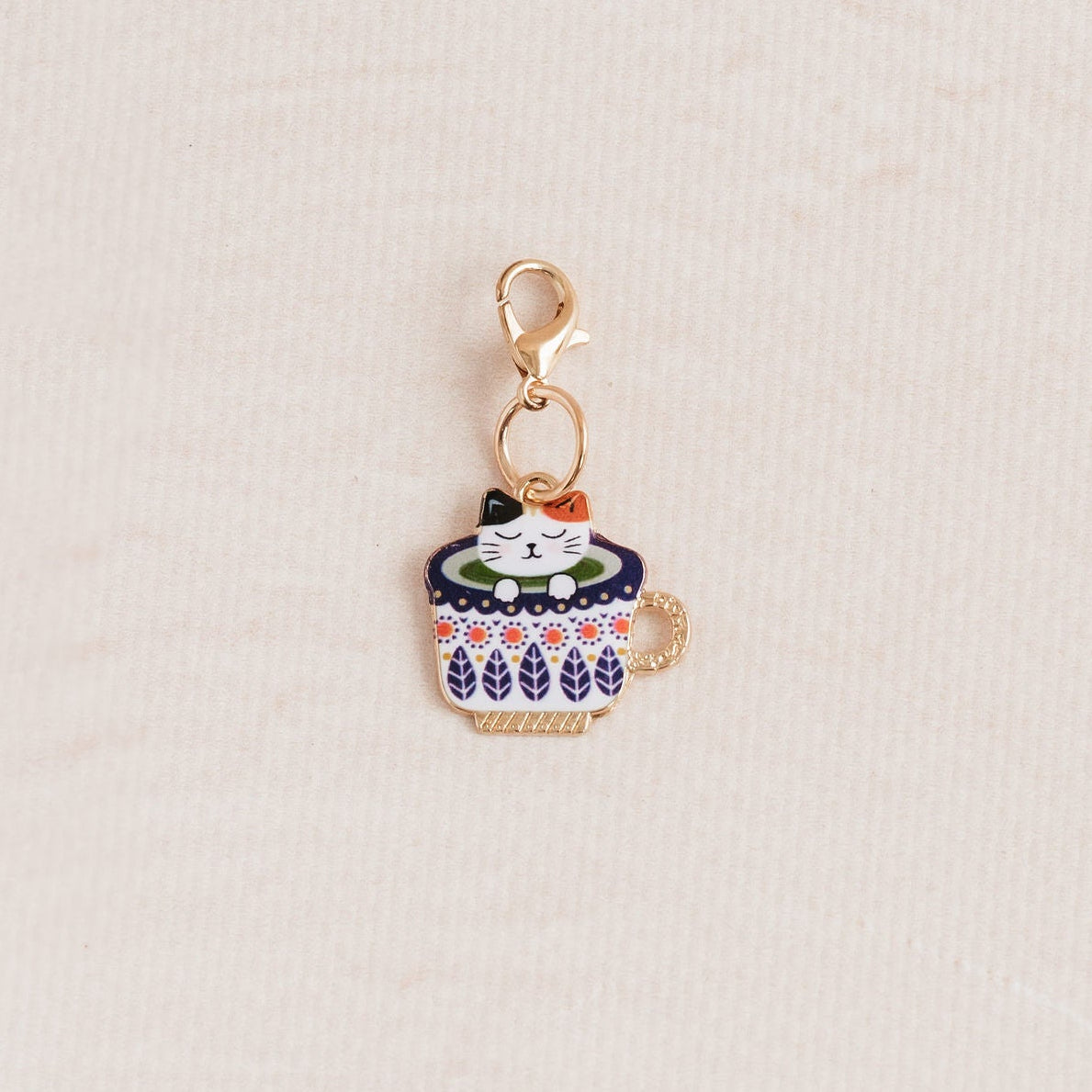 A small gold-tone charm shaped like a cupcake with colorful enamel details, photographed on a light textured background.