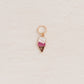 A small ice cream cone charm with a gold-tone ring at the top, featuring white and pink enamel detailing, placed on a textured off-white background.