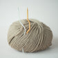 Ball of beige yarn with two metal hooks on a light gray background